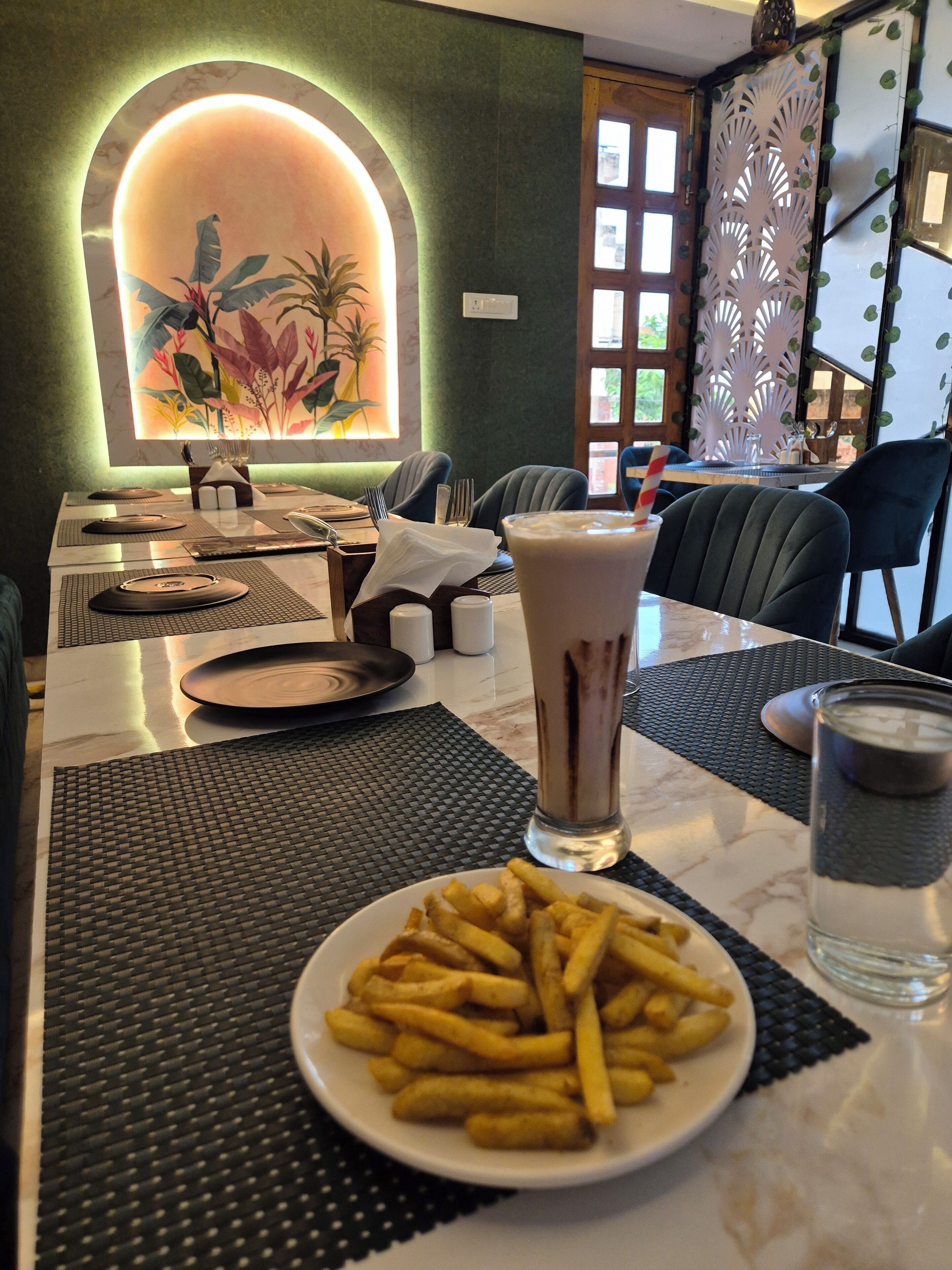 A dining area with a table set for two, featuring a plate of fries, a glass of water, and a tall drink.