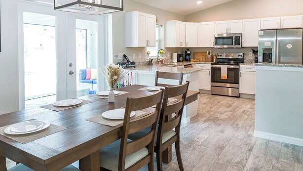 A modern kitchen with white cabinets, a wooden dining table, and a built-in oven. - Family Beach Retreat w/ Private Fenced Backyard, Fire Pit, Games (Englewood)