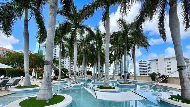 A pool area with palm trees, lounge chairs, and a clear blue sky.