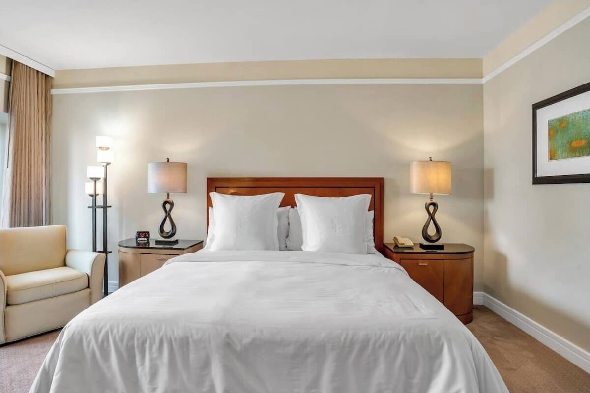 Una camera d'albergo con un letto grande, due comodini con lampade, una sedia e un quadro appeso al muro.