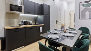 Una cocina moderna con armarios oscuros, un microondas de acero inoxidable y una cafetera. Hay una mesa de comedor con platos, vasos y un florero con flores.