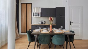 Un comedor con una mesa dispuesta para cuatro personas, rodeada de sillas verdes, una cocina moderna con armarios negros y una puerta blanca.
