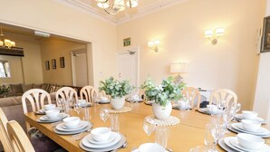 Un comedor con una mesa larga dispuesta para una comida, sillas alrededor y un letrero de salida de incendios en la pared.