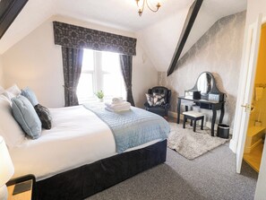 A bedroom with a bed, a desk, a chair, a mirror, and a window with curtains. - The Causeway (Llandudno)
