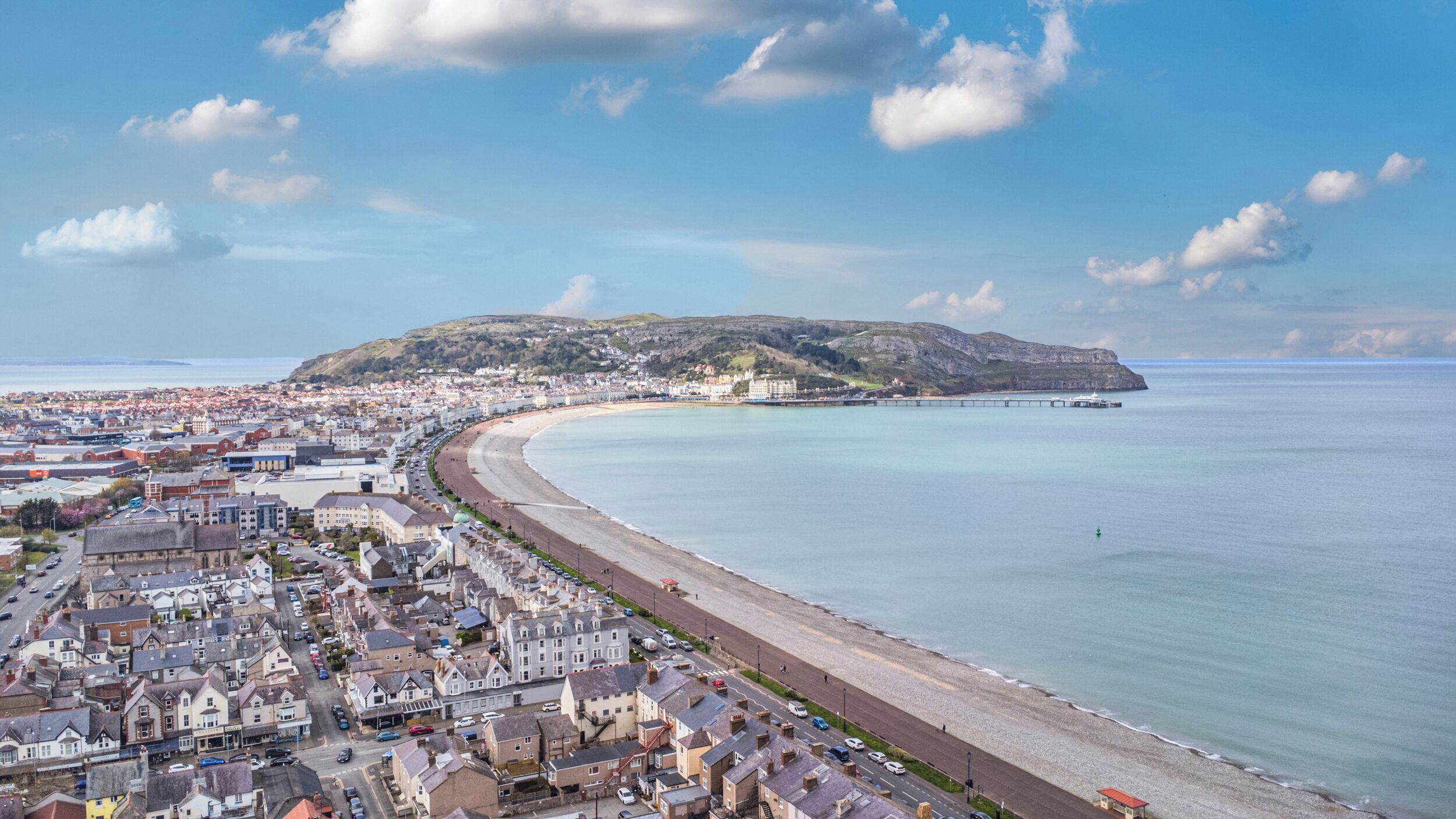 A coastal town with a beach, a pier, and a hill in the background.