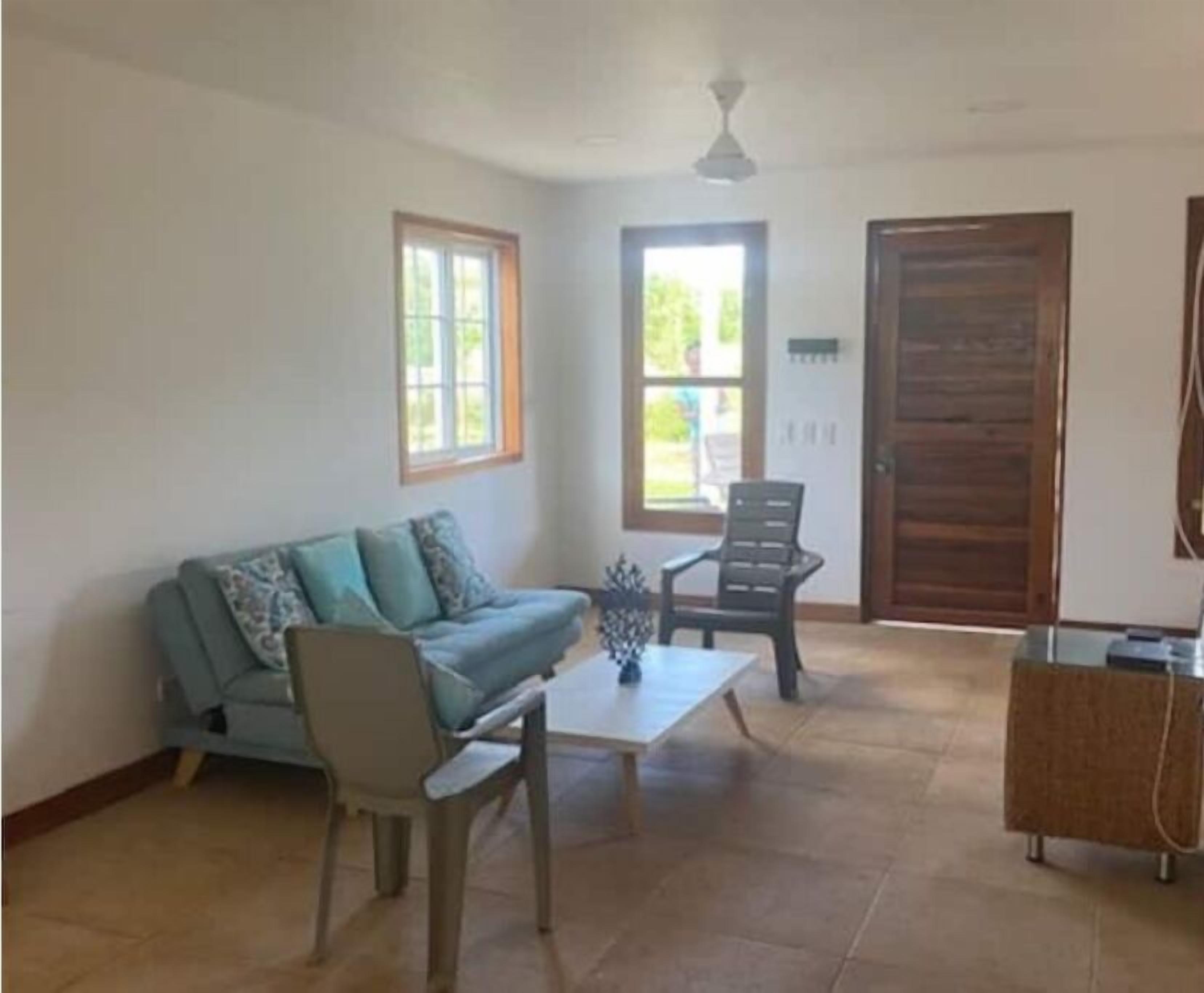 A spacious living room with a sofa, a coffee table, and a chair. There are windows and a door in the room.