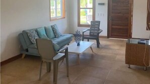 A spacious living room with a sofa, a coffee table, and a chair. There are windows and a door in the room. - Savannah House (San Andrés y Providencia)
