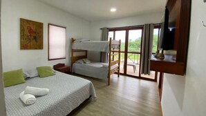 A bedroom with a bunk bed, a single bed, a desk, a chair, a TV, and a balcony with a view of greenery. - Savannah House (San Andrés y Providencia)