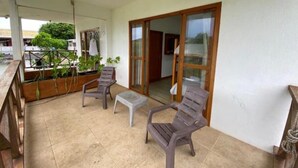A balcony with two plastic chairs and a small table, a wooden bench, and a potted plant area. - Savannah House (San Andrés y Providencia)