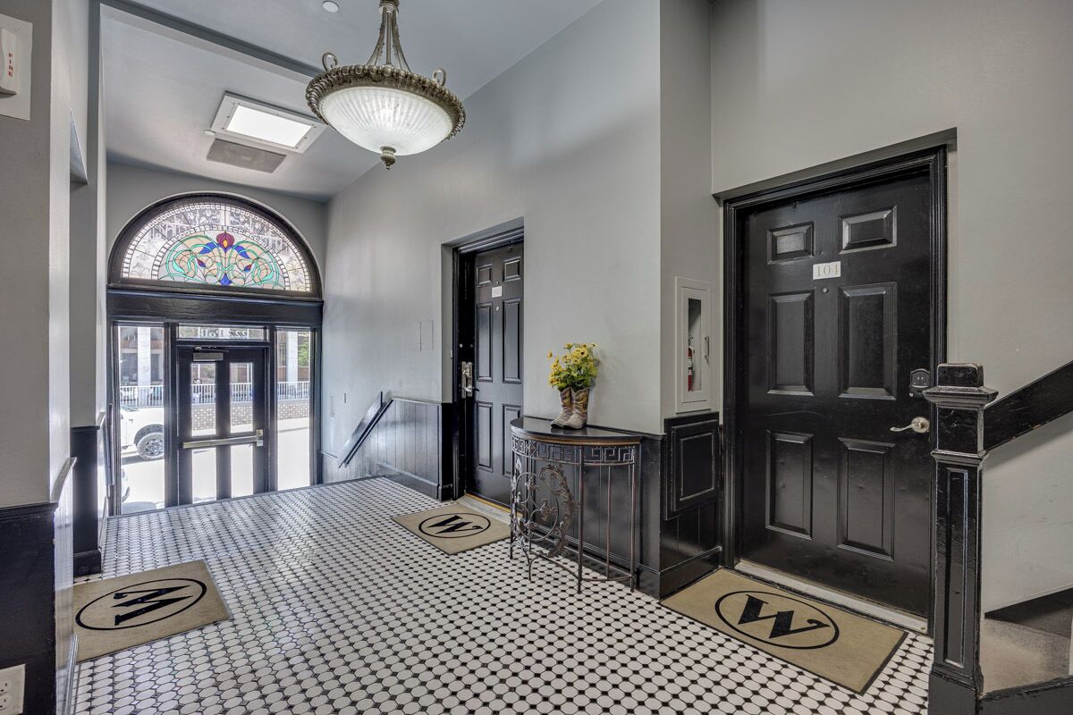 A hallway with a patterned floor, a chandelier, a door with a sign, and a stained glass window.