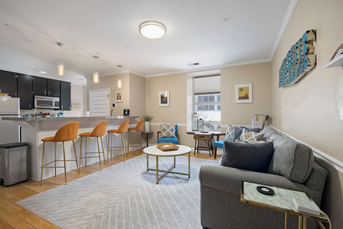 A modern living room with a gray sofa, a coffee table, and a kitchen area with bar stools.