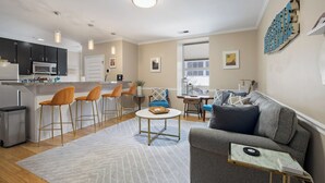 Ein modernes Wohnzimmer mit grauem Sofa, einem Couchtisch und einer Küchenzeile mit Barhocker.
