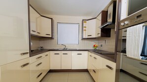 Una cocina moderna con armarios blancos, horno empotrado y ventana sobre el fregadero.