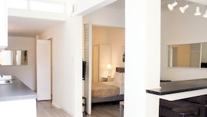 Een moderne hotelkamer met kitchenette, een bed met nachtkastje, zithoek met tafel en stoelen, en een grote spiegel.