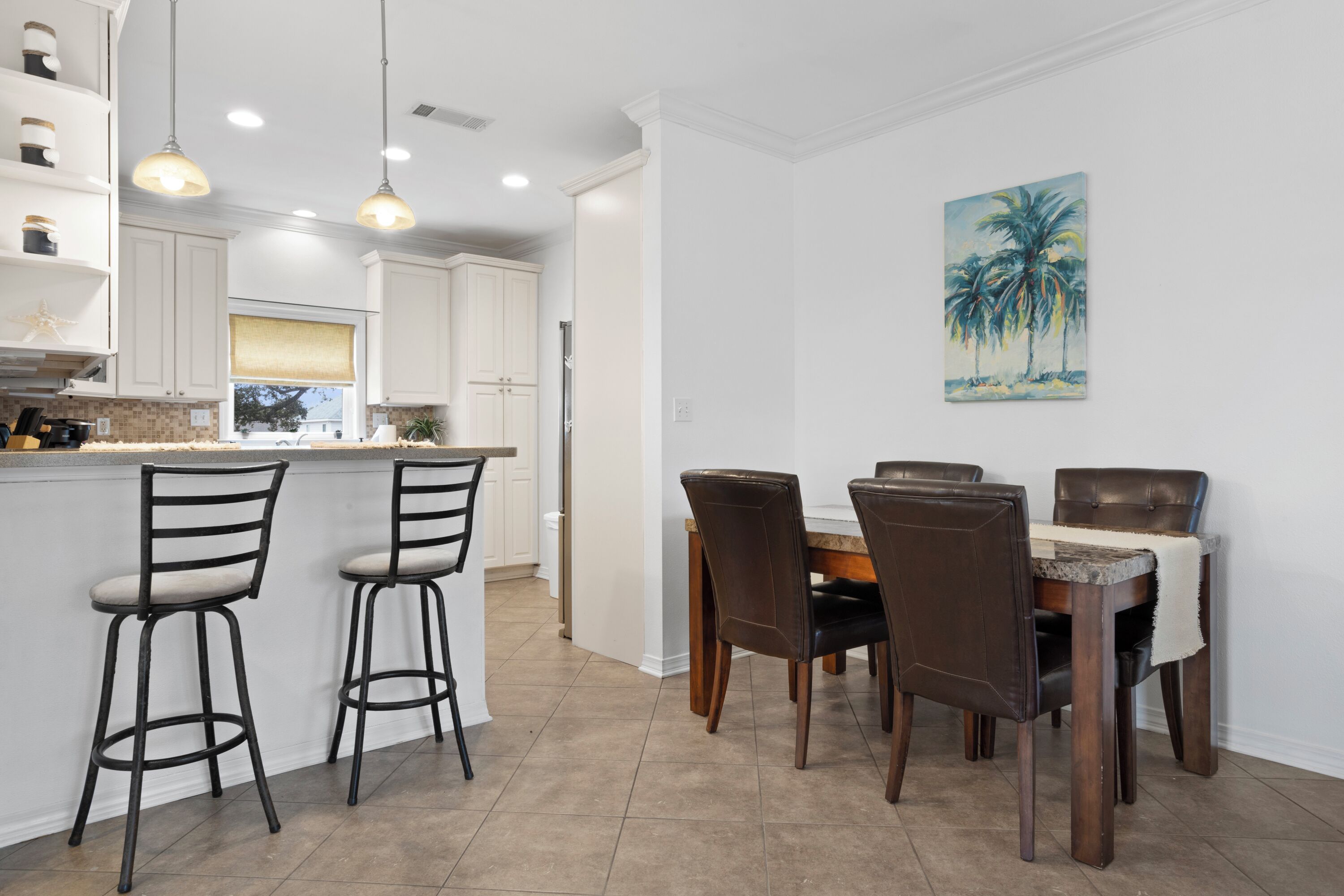 A kitchen with white cabinets, a dining area with a table and chairs, and a painting of palm trees on the wall.