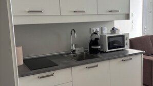 Una cocina moderna con armarios blancos, un lavamanos de acero inoxidable, un microondas y una cafetera.