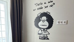 Una habitación con una butaca tapizada, una pequeña mesa negra y un adhesivo mural con un personaje de dibujos animados y texto.