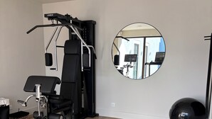 Un gimnasio con equipo de ejercicio, un espejo y una banca.