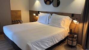 Una cama bien hecha con sábanas blancas, dos lámparas de noche y un espejo montado en la pared.