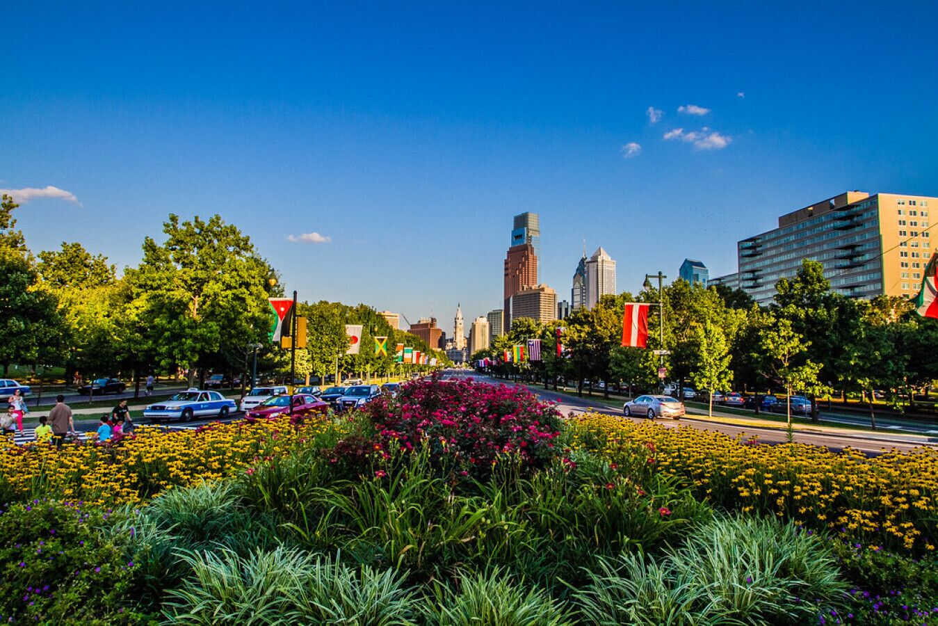 Un paisaje urbano con un edificio destacado, una calle concurrida y un jardín de flores.