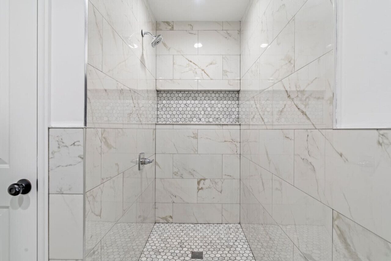 A walk-in shower with white marble tiles and a hexagonal tile pattern on the floor.