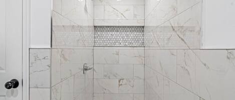 A walk-in shower with white marble tiles and a hexagonal tile pattern on the floor.