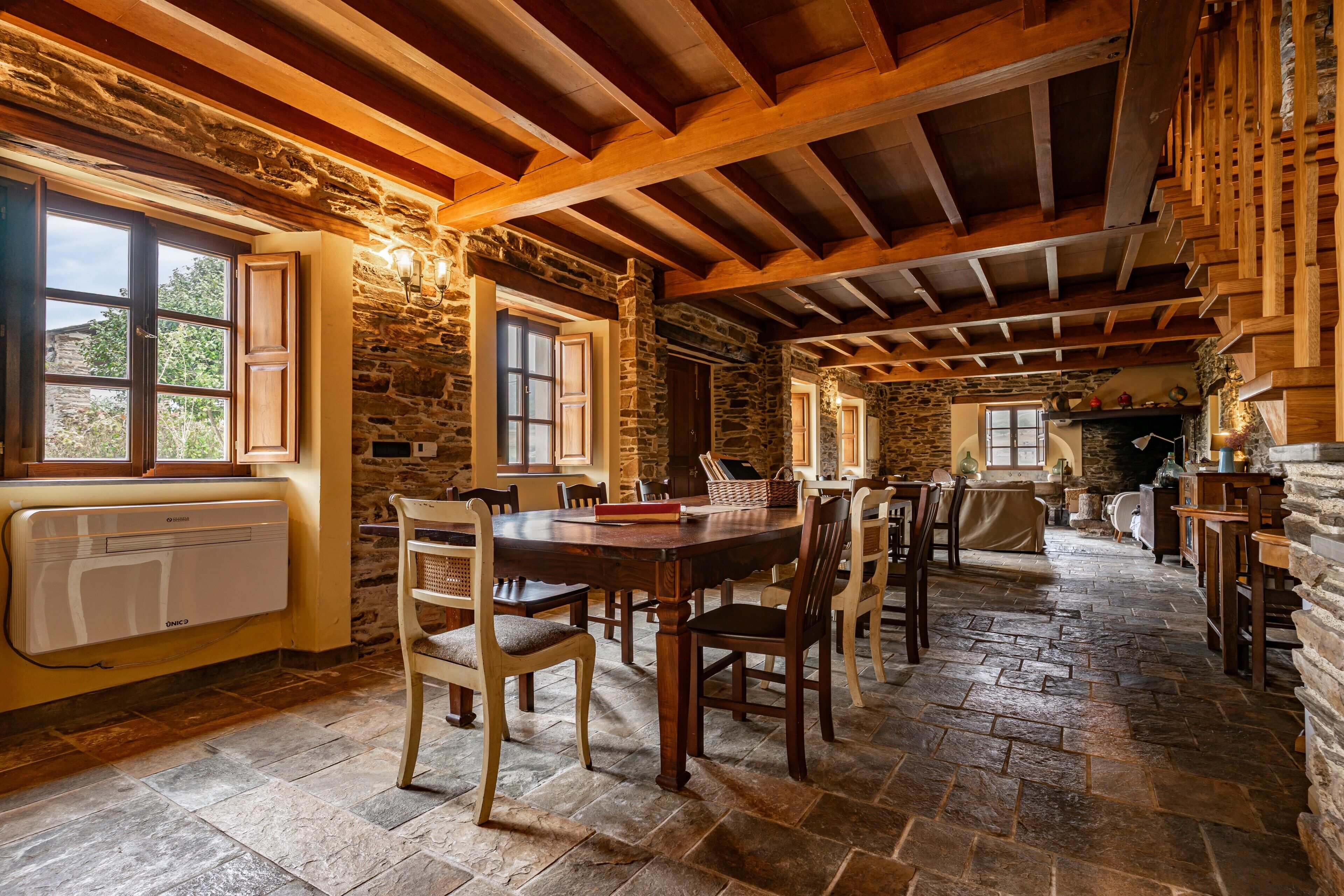 A rustic interior with stone walls, wooden beams, a dining table with chairs, and a fireplace.