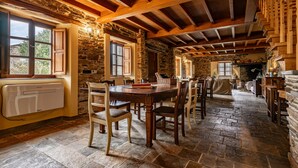 Un intérieur rustique avec des murs en pierre, des poutres en bois, une table à manger avec des chaises et une cheminée.