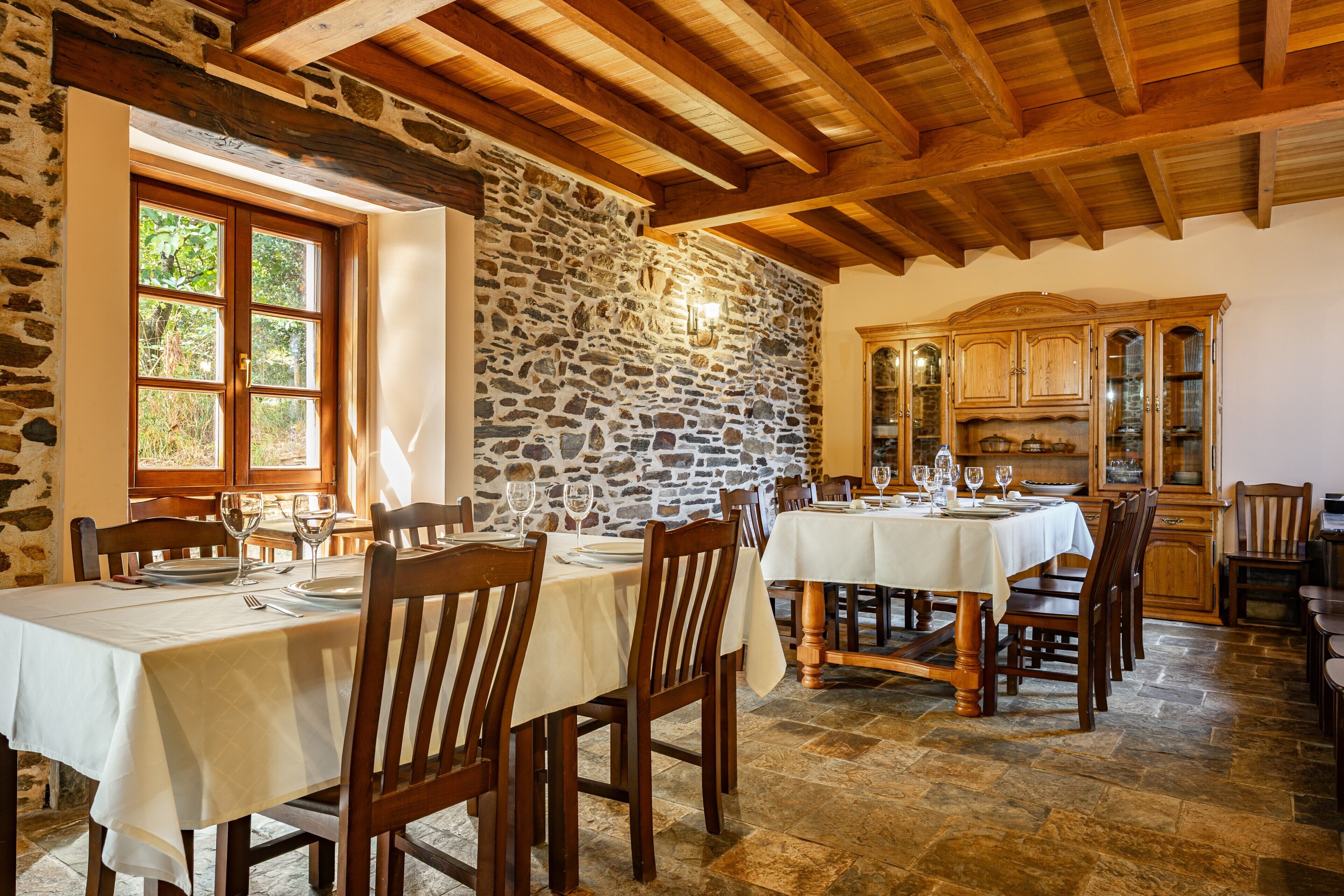 A dining area with stone walls, wooden beams, and tables set for dining.