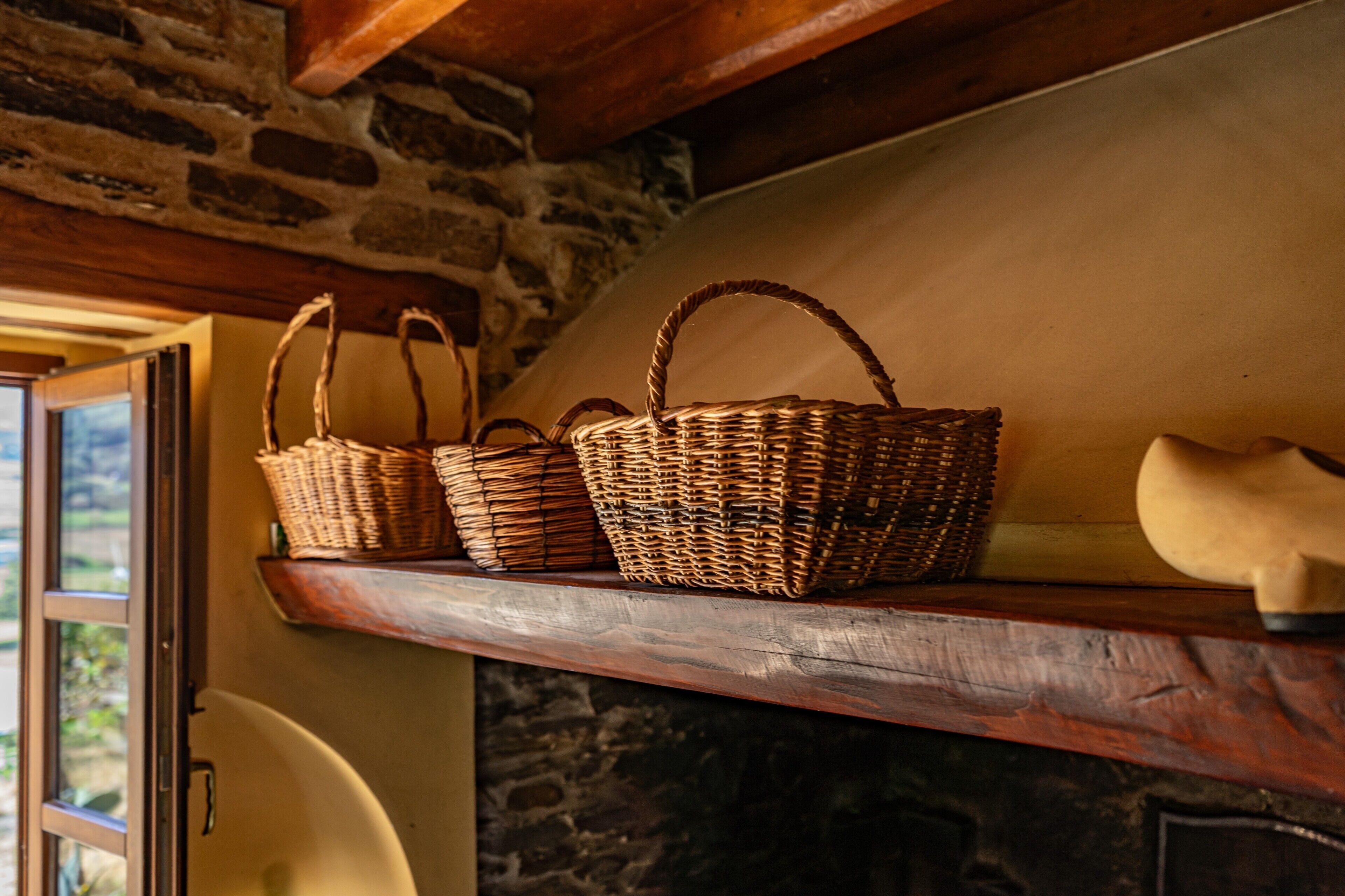 Des paniers en osier sur une étagère en bois, un mur de pierre et une porte donnant sur l’extérieur.