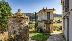 Un edificio de piedra con una pequeña torre, un camino pavimentado y una zona verde con árboles.