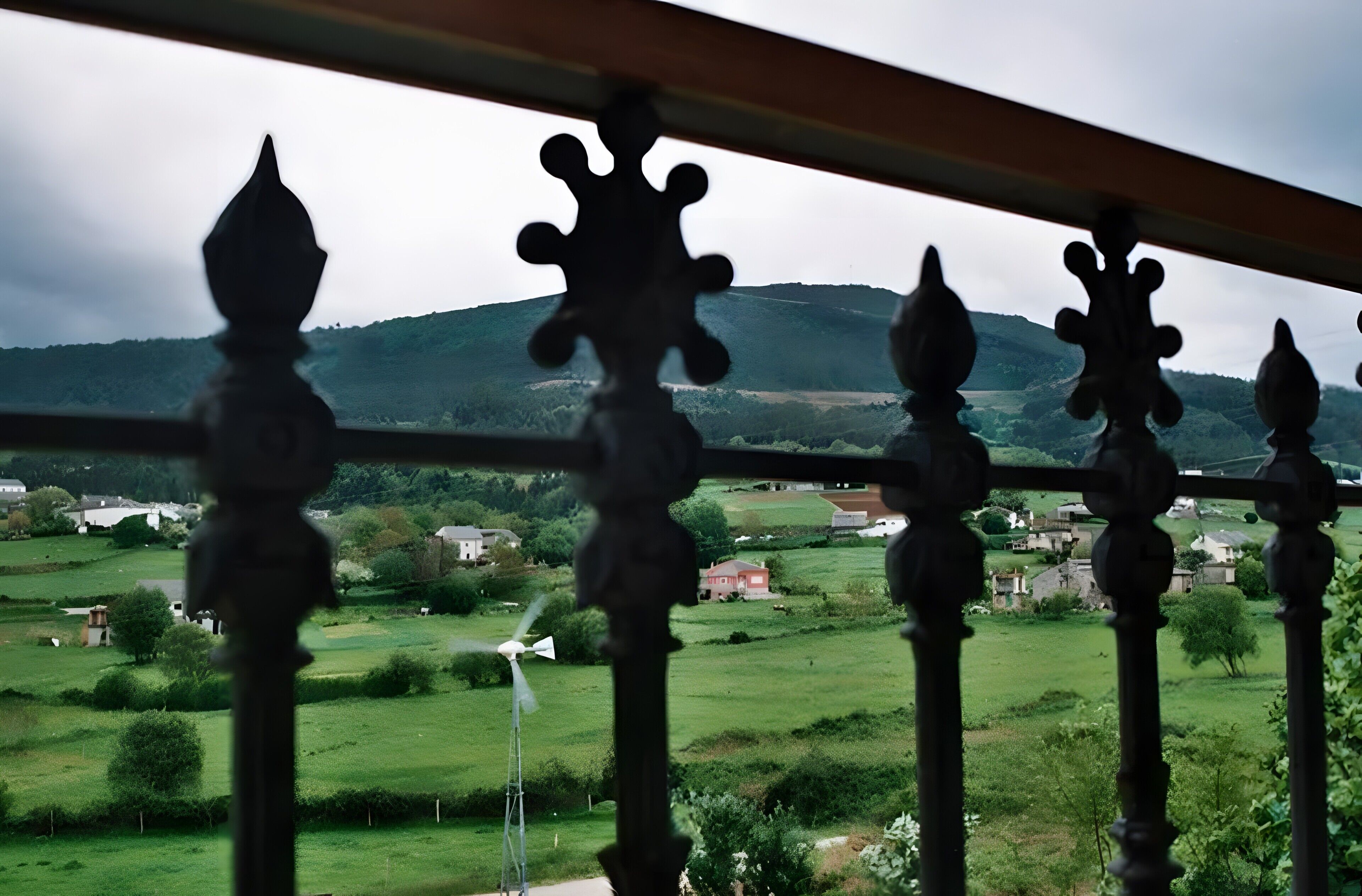 A balcony with ornate balusters overlooking a rural landscape with houses and wind turbines.