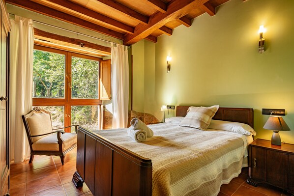 Une chambre à coucher avec un grand lit, une chaise, une table de chevet et une fenêtre avec des rideaux.