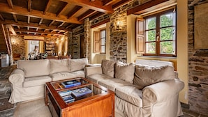 A cozy room with a stone wall, wooden beams, a beige sofa, and a coffee table with books.