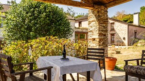 An outdoor patio with a table set for two, surrounded by wooden chairs and a stone pillar.
