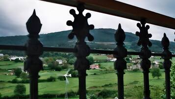 Un balcón con barandilla decorativa que da a un paisaje rural con casas y aerogeneradores.