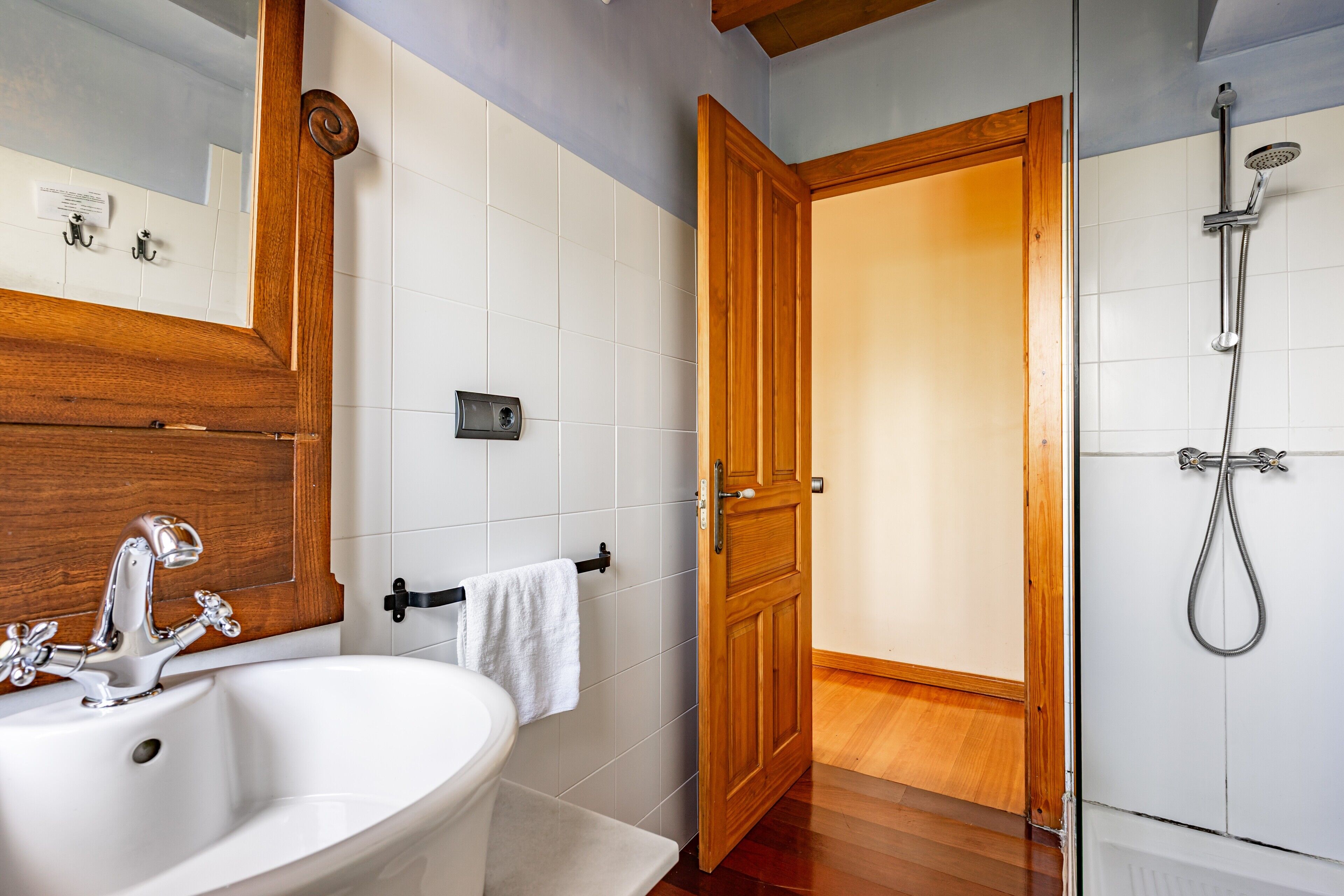 Un baño con un lavabo blanco, puerta de madera y ducha.