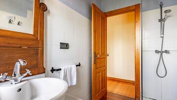Un baño con un lavabo blanco, puerta de madera y ducha.