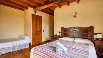 Un dormitorio con techo de madera, una cama grande con colcha a rayas de colores, una cama más pequeña, mesitas de noche de madera y una puerta de madera.