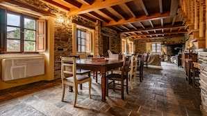 A rustic interior with stone walls, wooden beams, a dining table with chairs, and a fireplace.