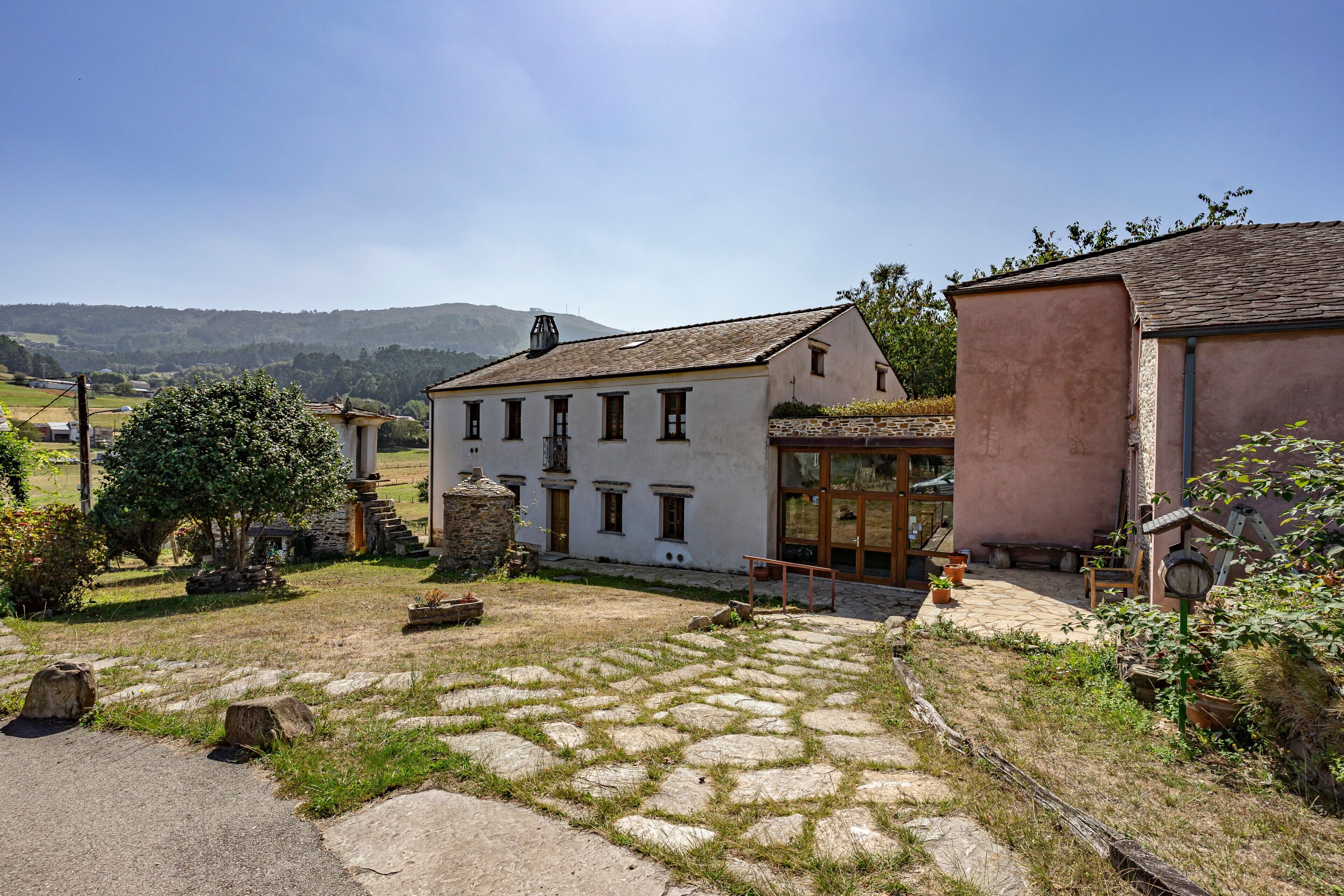 Un patio de piedra tradicional con un edificio blanco, escalones de piedra y un banco de madera.