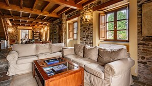 A cozy room with a stone wall, wooden beams, a beige sofa, and a coffee table with books.