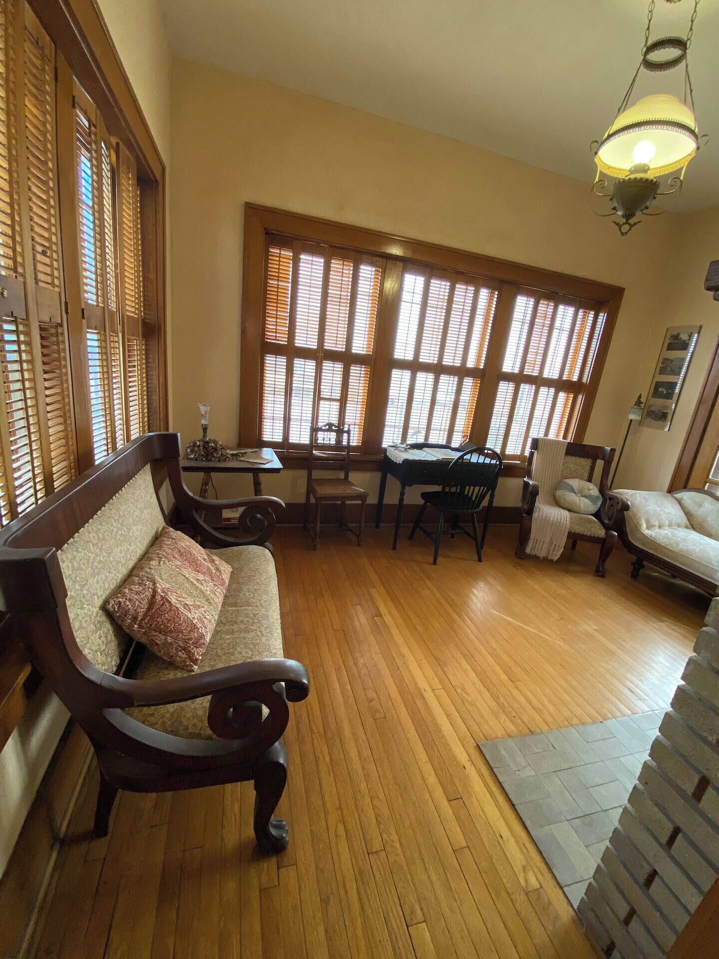 A spacious room with a wooden floor, a sofa, a dining table with chairs, and large windows with blinds.