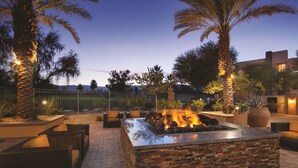 An outdoor patio with a stone fire feature, wicker furniture, and palm trees. - Marriott Shadow Ridge The Enclaves COACHELLA STAGECOACH (Palm Desert)