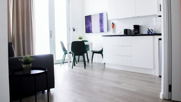Une cuisine moderne avec des meubles blancs, un coin repas comprenant une table et des chaises, et une petite table d’appoint agrémentée d’une plante.