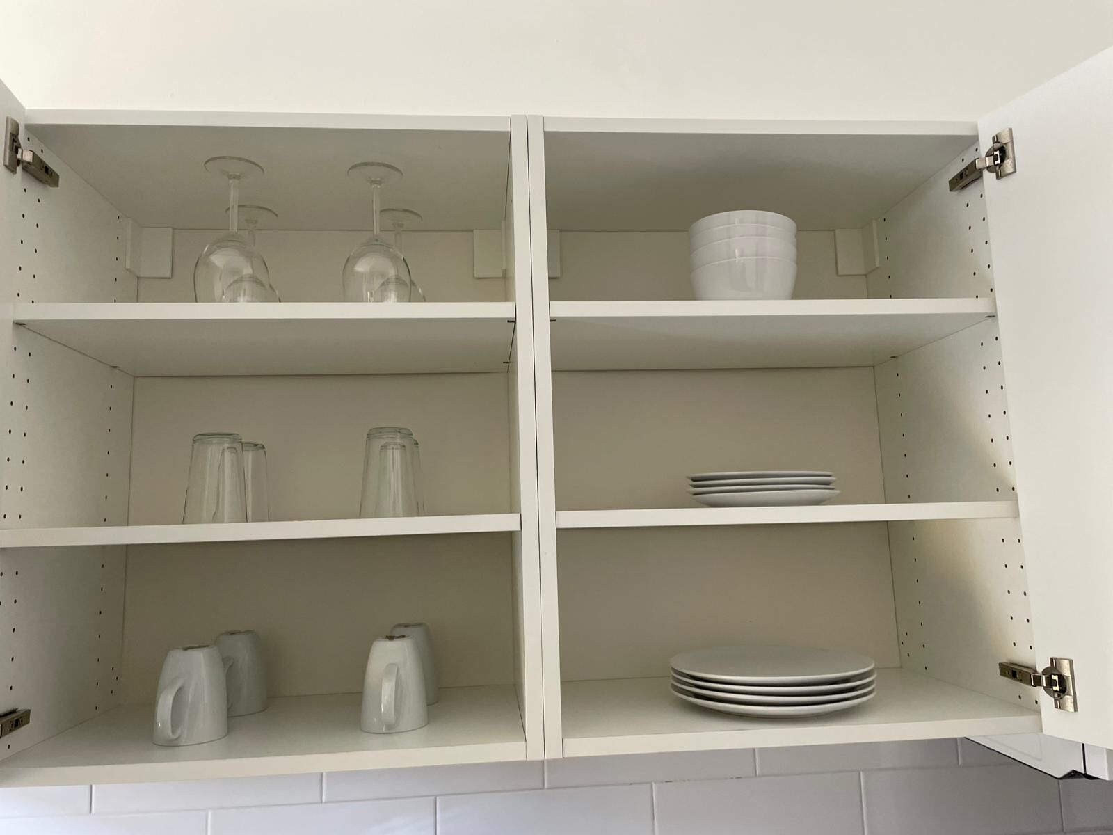 Een witte kast met drie planken, elk gevuld met verschillende keukenbenodigdheden.