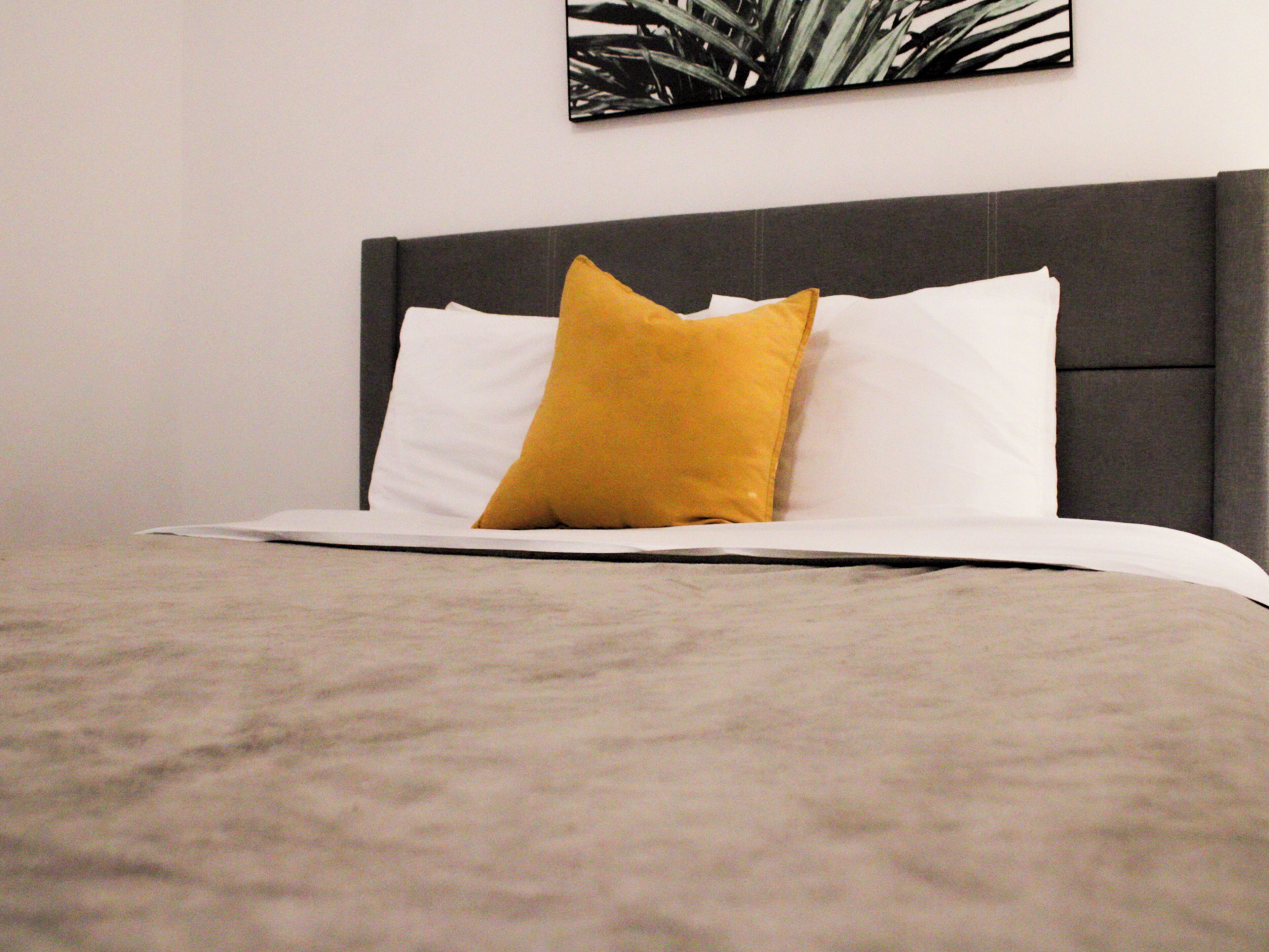 A bed with a grey headboard, white and yellow pillows, and a grey bedspread.
