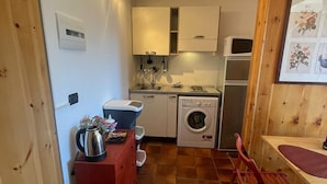 Una cocina pequeña con electrodomésticos básicos, una silla roja y un armario de madera.