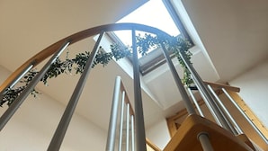 Una escalera con barandilla de madera y balaustradas de metal, que conduce a una habitación con tragaluz y una planta colgante.