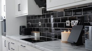 A modern kitchen with white cabinets, black tiled backsplash, and a built-in oven. - Stylish 3-Bed • Hot Tub • Free Parking • Contractors (Essex)